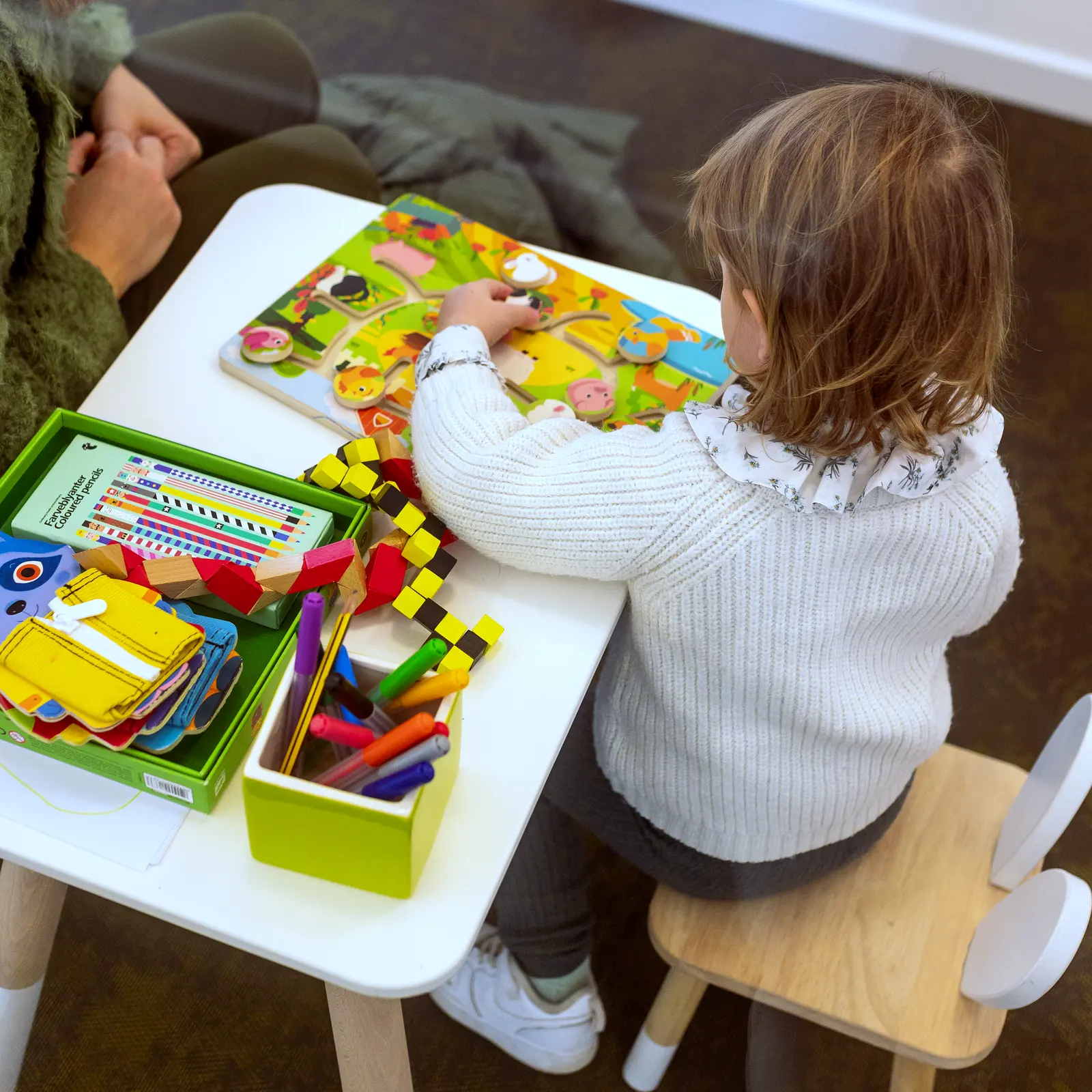 L'angolo dei bambini dello studio: una bambina di spalle gioca al tavolino coi colori e le costruzioni, accanto a lei le mani di un'adulta.