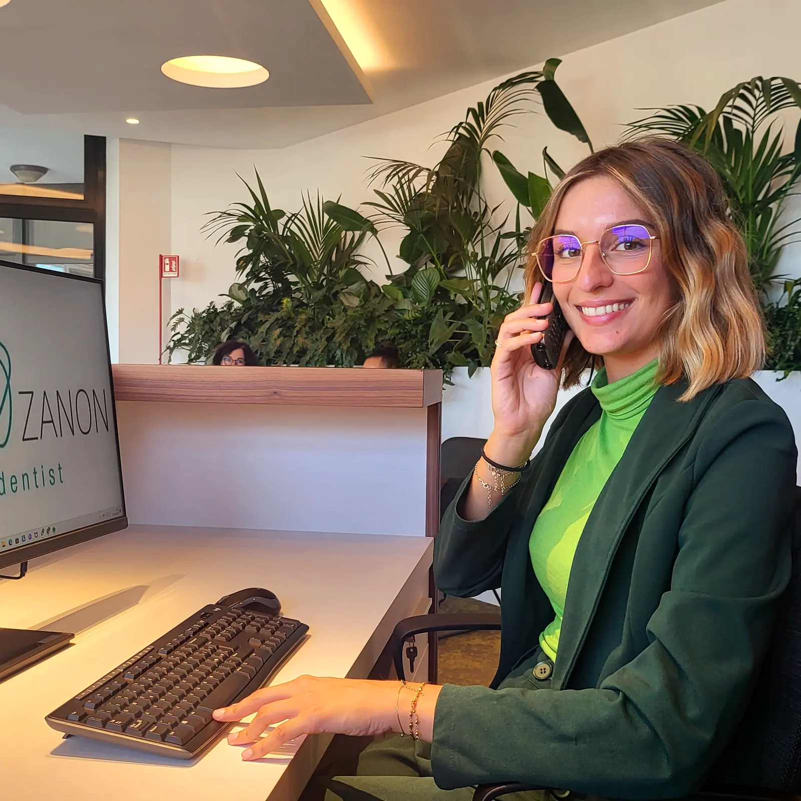 La segreteria al telefono, alla scrivania dell'accoglienza; sullo schermo il marchio dello studio.